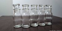Front view of five clear glass bottles with stoppers