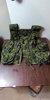 Front view of green digital camo tactical vest laid flat showing pouches and zipper