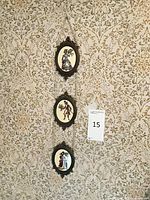 Three oval framed embroidery pieces connected by chains hanging on wall