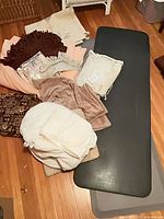 Lot overview showing stacked black and grey anti-fatigue mats, surrounding pillows, blankets and throws