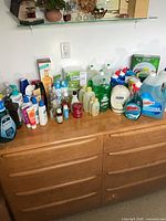 Overview of approximately 25 assorted cleaning supplies and toiletries on dresser