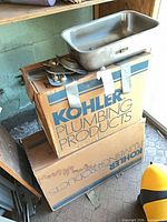 Two Kohler boxes with stainless steel sink resting on top alongside brass hardware pieces