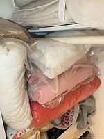 Multiple folded and bagged comforters, blankets, pillow inserts in closet shelf