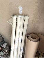 Six rolled vinyl roller shades with chain mechanisms leaning against wall