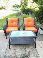Full view of two resin wicker chairs with orange cushions and matching glass-top coffee table