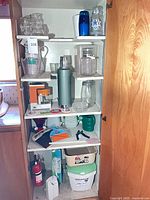 Full cabinet view showing thermoses, glassware, jars, coasters, dustpan, tools, compost bin and dishpan