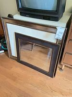 Two dark brown wood-framed mirrors leaning against furniture