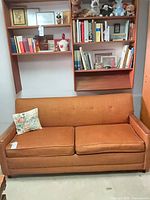 Full view of burnt orange mid-century Simmons sofa with bookshelf backdrop