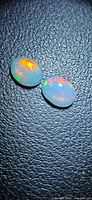 Pair of oval opals showing red, green and orange flashes on black background