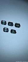 Five octagon-cut blue-green sapphires laid out on white background