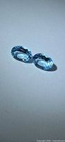 Pair of oval blue topaz gemstones on neutral background