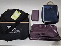 All four bags laid out: black TX Canada bag, navy Dior bag, metallic purple pouch, small purple wallet