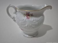 Full view of white porcelain creamer with floral design and gold rim