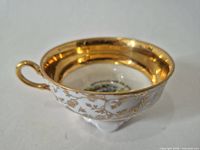Side view of teacup showing gold interior, white exterior with gilt pattern, handle