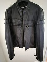 Front view of black leather biker jacket hanging, shows full design and brand tag