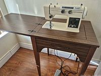Sewing machine installed in wood laminate cabinet with foot pedal visible