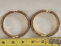 Two gold plated rhinestone bangles beside ruler for scale
