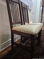 Side view of both dark wood chairs showing slat backs and cream damask seats