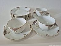 Set showing three teacups with saucers and stack of dessert plates