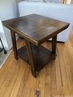 Angle view of one dark brown end table showing top, legs and lower shelf