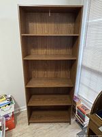 Full front view of tall brown engineered wood bookcase with five shelves
