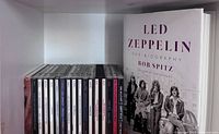 Row of sixteen Led Zeppelin CD jewel cases beside hardcover biography book