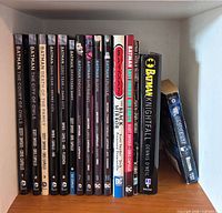 Spines of 14 Batman graphic novels and sampler on shelf