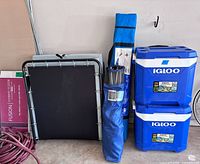 Group shot showing two Igloo coolers, two folded cots, chair bag, garden hose, flooring box