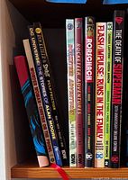 Shelf showing DC Universe: The Stories of Alan Moore, Rocketeer Adventures vols.1-2, Rorschach, Flash Impulse, Green Lantern/Green Arrow, The Death of Superman and one blue hardcover