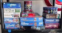 All puzzle and game boxes arranged on shelf showing titles, piece counts and tin packaging