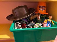 Green bin containing Woody hat, Woody and Buzz figures, Cars traffic cone, small vehicles