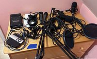 Entire podcasting kit spread on dresser including microphones, boom arms, audio recorder, audio interface, headphones, cables