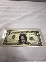 Front of modified 1977 Series $1 bill showing Elvis Presley portrait and serial number L93535957S in plastic sleeve