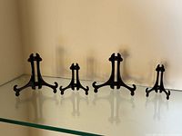 Four black easel stands of varying sizes on glass shelf