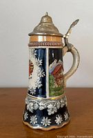 Full view of beer stein showing pewter lid, handle and decorative panels