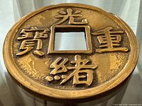 Front view of brass trivet showing square center hole and raised Chinese characters