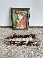 Framed hooked rug portrait leaning on wall, wool tassel wall hanging on floor