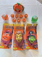 Overview of all items on table: three packaged doorbells, plush pumpkin, eight mini pumpkins, two jar lights