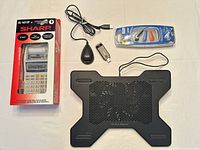 Group shot of all five items: boxed calculator, cooling pad, Wi-Fi adapter, USB cradle, packaged earbuds