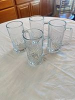 Four clear diamond-cut glass beer mugs grouped