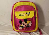 Front view of pink and yellow Mickey Mouse backpack showing graphic, front pocket, zipper