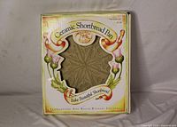 Front view of boxed Brown Bag Cookie Art Ceramic Shortbread Pan showing pan pattern and packaging text