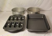 Four baking pans laid out: two round, one 9x13 rectangle, one 8-cavity twinkie pan