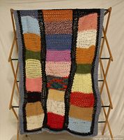 Full view of hand knitted multicolour patchwork blanket on rack