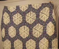 Full view of hand-knitted afghan showing cream and multicolor hexagon pattern