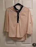 Front view of peach blouse with black collar hanging on hanger