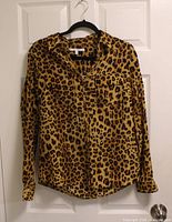 Front view of leopard print Alfred Sung blouse on hanger showing collar, pockets, sleeves and hem