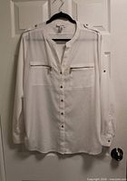 Front view of white Calvin Klein blouse showing gold buttons, zip pockets, epaulets, roll-tab sleeves