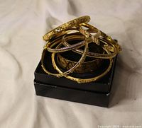 Stack of seven assorted gold-tone bangles on black box