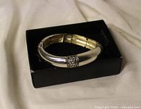 Silver-tone hinged bracelet resting in black box, showing exterior finish and decorative panels